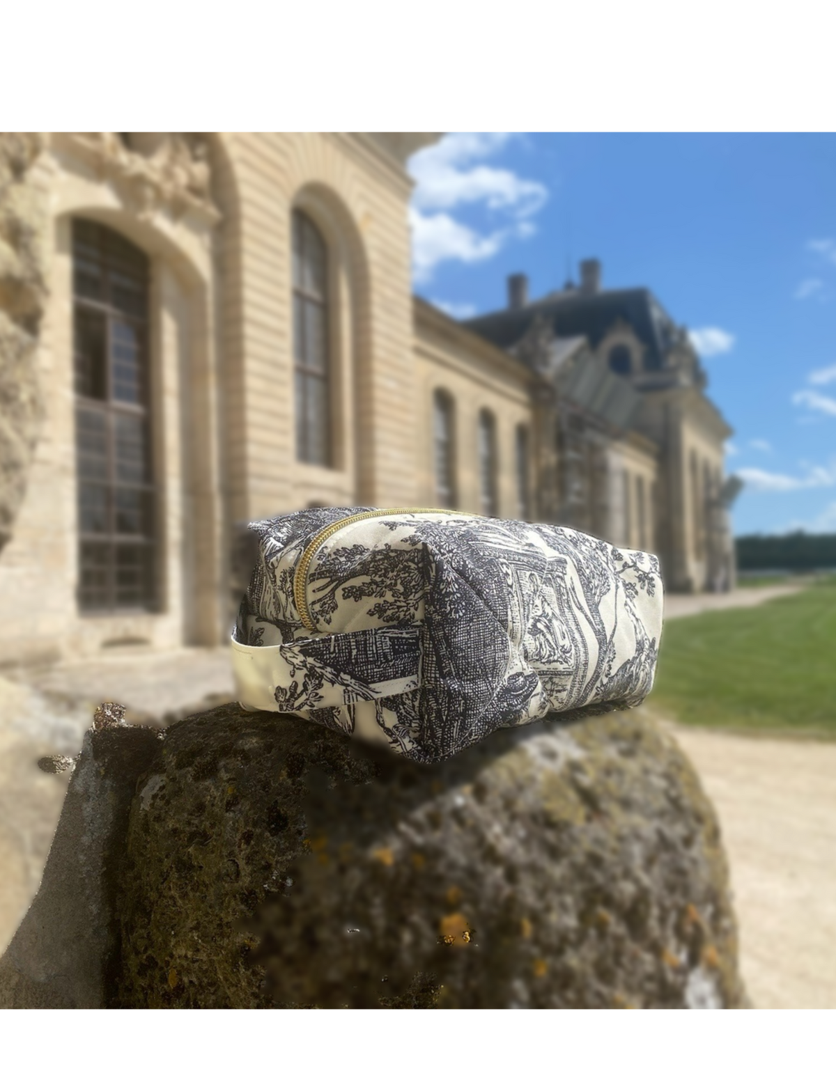 Washbag in toile de Jouy from the Château Mont Royal, resting on a stone in front of a château façade